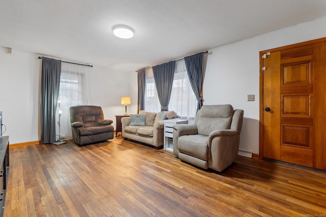 living area with baseboards, wood-type flooring, a baseboard heating unit, and a wealth of natural light