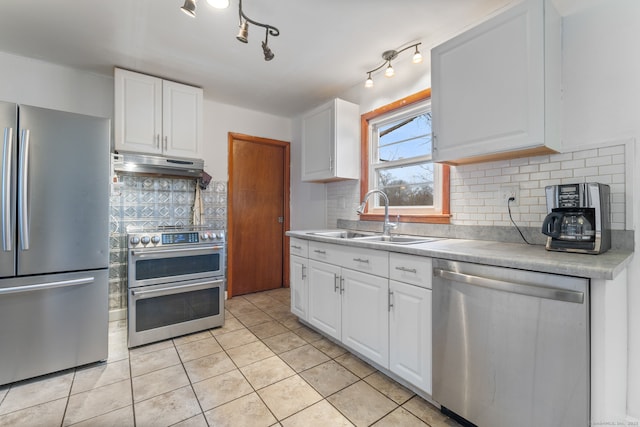 kitchen with stainless steel appliances, tasteful backsplash, white cabinetry, a sink, and under cabinet range hood