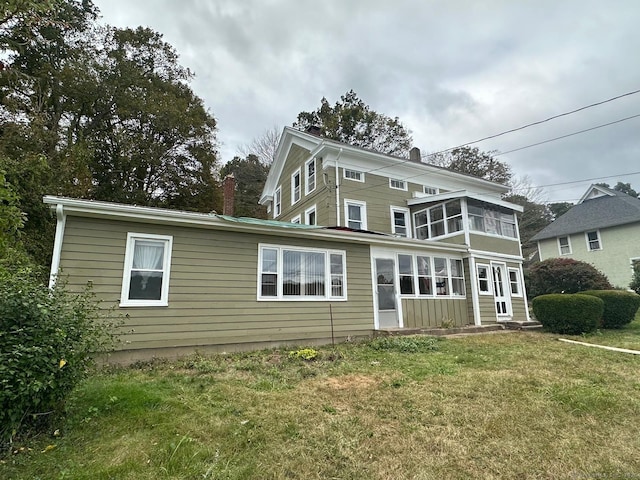 rear view of house with a lawn, a chimney, and a sunroom