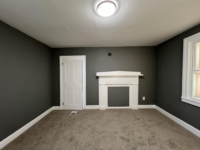 unfurnished living room with carpet floors, a fireplace, visible vents, and baseboards