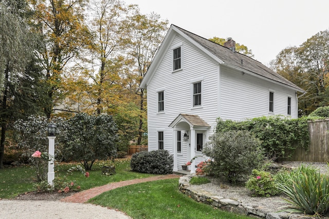 traditional-style home with entry steps, fence, a chimney, and a front yard