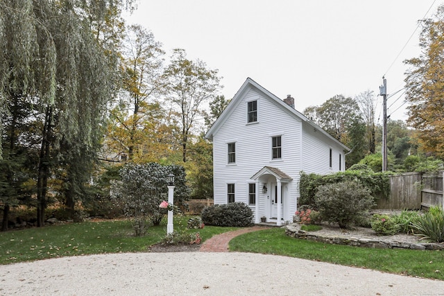 traditional-style house with a chimney, fence, and a front yard