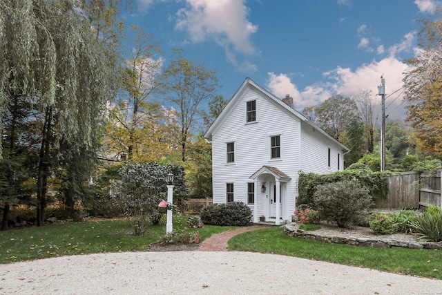 traditional-style house featuring a front lawn, a chimney, and fence