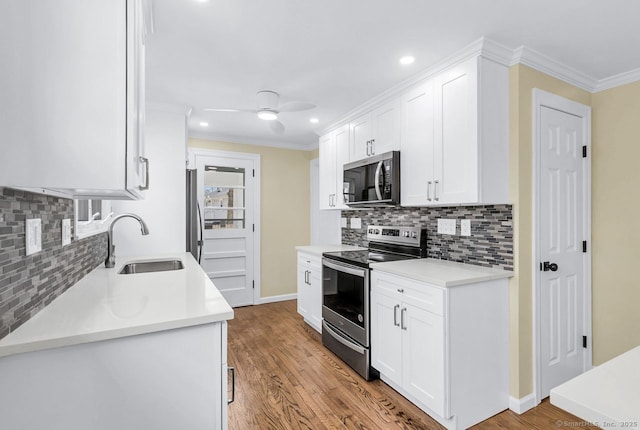 kitchen with light countertops, appliances with stainless steel finishes, ornamental molding, white cabinets, and a sink