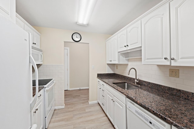 kitchen with white appliances, white cabinets, dark stone countertops, light wood-type flooring, and a sink