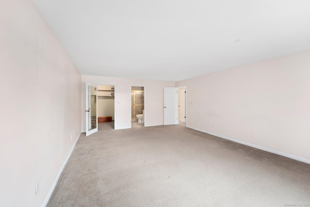 unfurnished bedroom featuring baseboards, a closet, a walk in closet, and light colored carpet