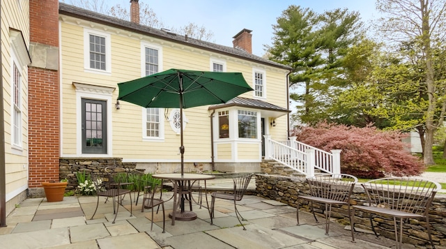 rear view of property with outdoor dining space, a patio, and a chimney