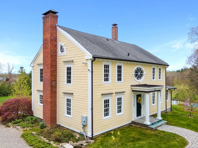 rear view of house featuring a shingled roof, a chimney, and a yard