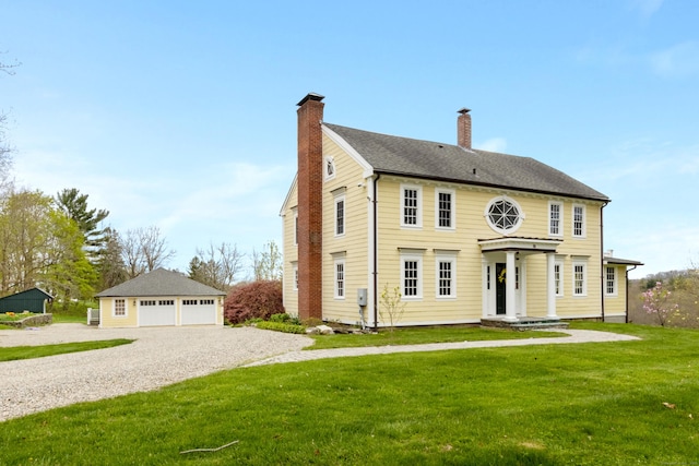 view of front of property with a garage, a shingled roof, an outdoor structure, a front lawn, and a chimney