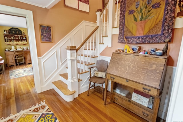 staircase featuring a decorative wall, wood finished floors, and wainscoting