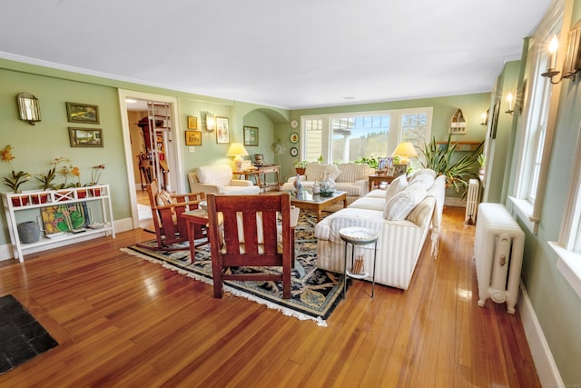 living area with arched walkways, baseboards, radiator heating unit, and wood finished floors