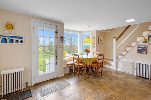 dining area featuring stone tile flooring, radiator, and stairs