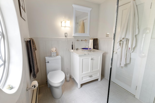 bathroom featuring a wainscoted wall, vanity, toilet, and walk in shower