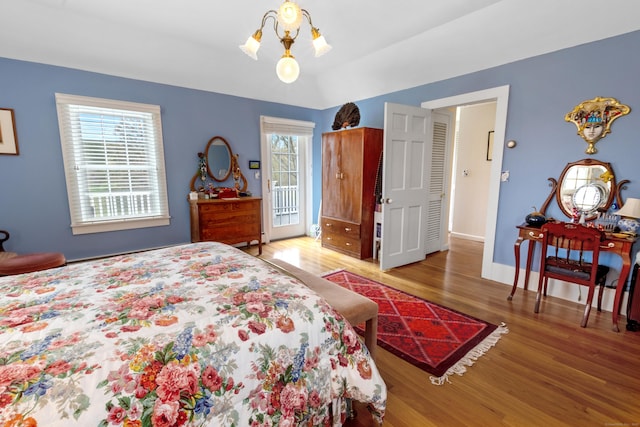 bedroom featuring access to exterior, baseboards, a chandelier, and wood finished floors