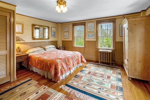 bedroom with ornamental molding, radiator heating unit, wainscoting, and wood finished floors