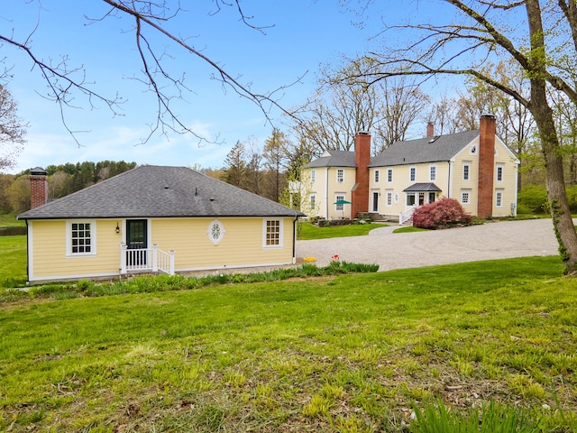 back of house featuring driveway, a chimney, and a yard