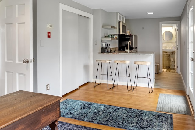 kitchen with light wood-style flooring, stainless steel microwave, a kitchen breakfast bar, light stone counters, and freestanding refrigerator