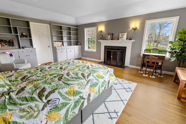 bedroom with multiple windows, light wood-type flooring, a fireplace, and baseboards