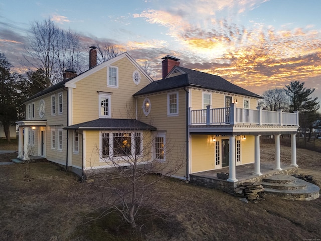 back of house at dusk with a deck, a patio, and a chimney