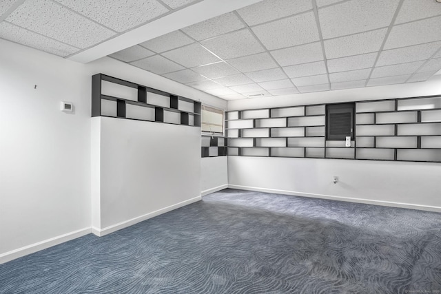 empty room with dark colored carpet, a drop ceiling, and baseboards