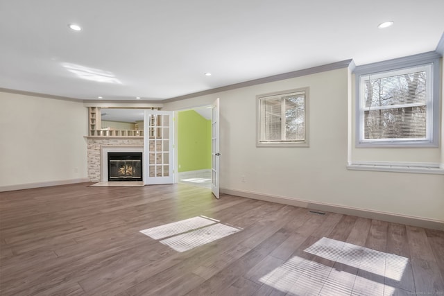 unfurnished living room featuring ornamental molding, a fireplace with flush hearth, baseboards, and wood finished floors