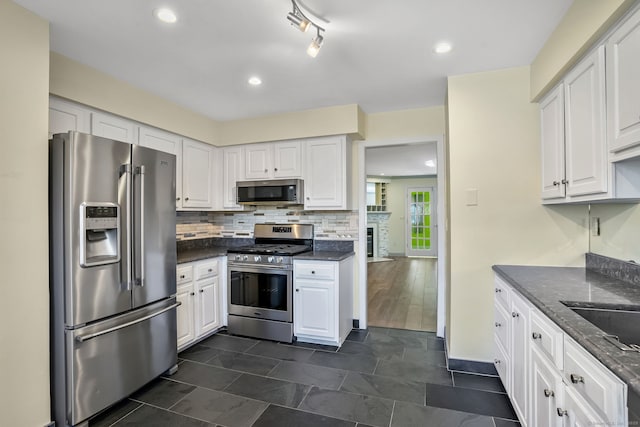 kitchen with stainless steel appliances, dark stone countertops, backsplash, and white cabinets