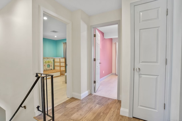 hall featuring light wood-style flooring, visible vents, baseboards, and an upstairs landing