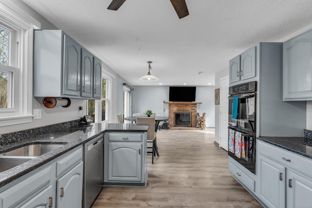 kitchen with light wood finished floors, dobule oven black, a brick fireplace, open floor plan, and dishwasher