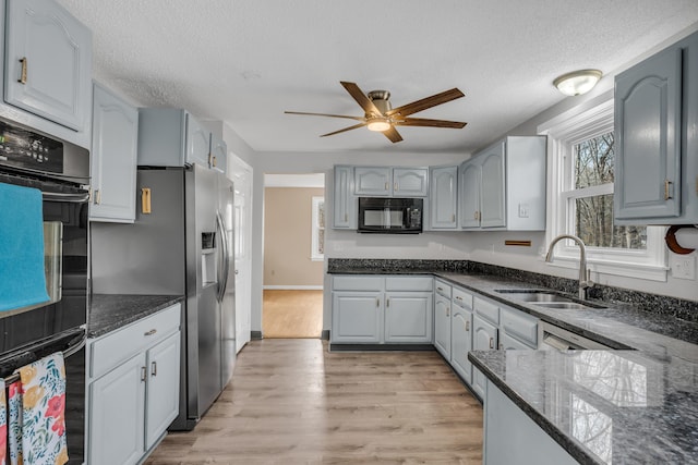 kitchen with a textured ceiling, light wood-style flooring, a sink, dark stone counters, and black appliances