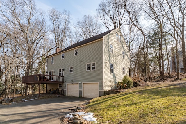 view of property exterior featuring a lawn, a chimney, aphalt driveway, an attached garage, and a deck