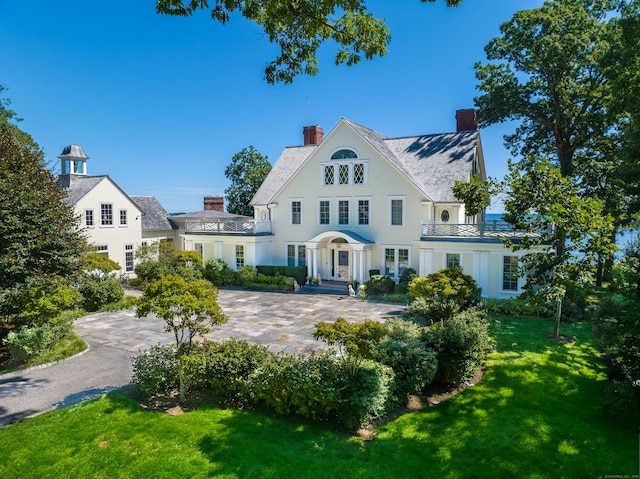 view of front of home with a balcony, a chimney, and a front yard