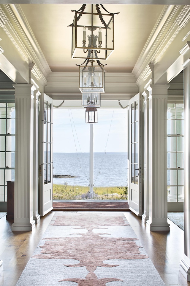 interior space with a water view, ornamental molding, decorative columns, an inviting chandelier, and wood finished floors