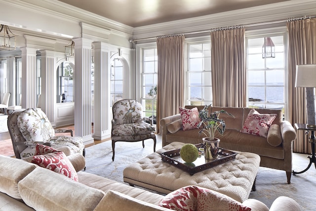 living area with crown molding, decorative columns, wood finished floors, and a water view