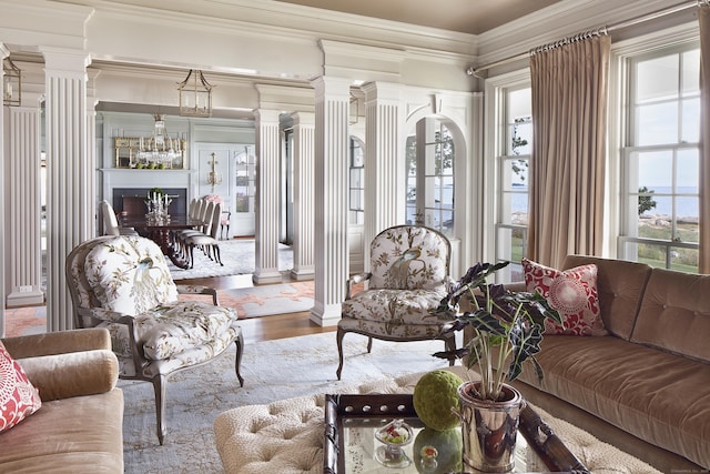 living area featuring decorative columns, wood finished floors, and crown molding