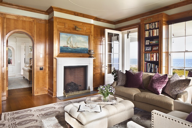 living area featuring a fireplace with flush hearth, dark wood-type flooring, arched walkways, wooden walls, and crown molding