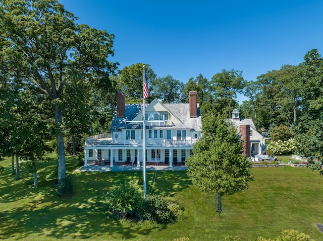 back of house with a patio, a balcony, a lawn, and a chimney