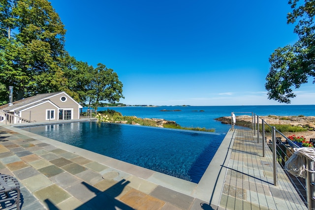 view of swimming pool featuring a storage structure, an infinity pool, a water view, and an outdoor structure