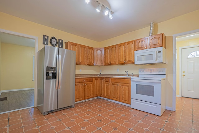 kitchen with brown cabinets, light countertops, a sink, white appliances, and baseboards