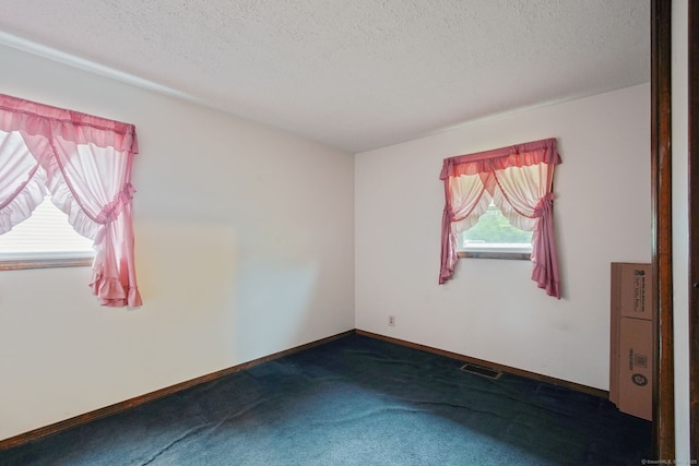 empty room with a textured ceiling, baseboards, visible vents, and dark carpet