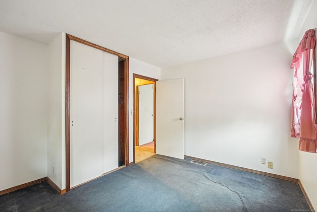 unfurnished bedroom featuring a closet, a textured ceiling, visible vents, and dark carpet