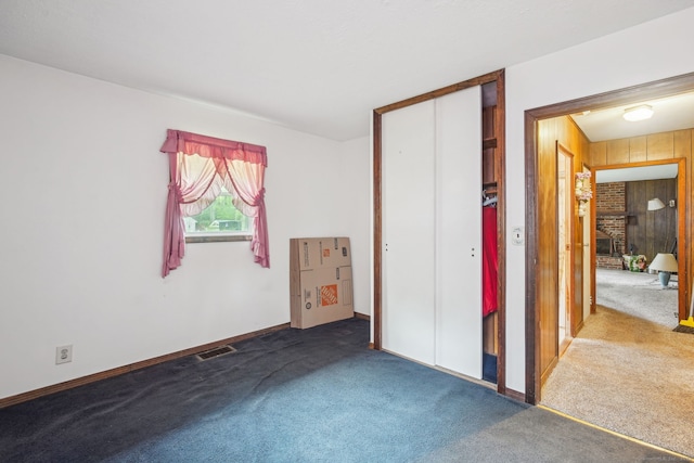 unfurnished bedroom featuring carpet, wooden walls, baseboards, and visible vents