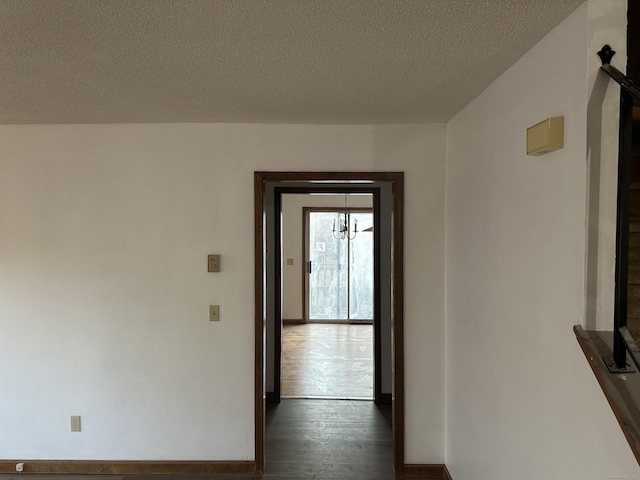 corridor featuring a textured ceiling, baseboards, and dark wood-type flooring