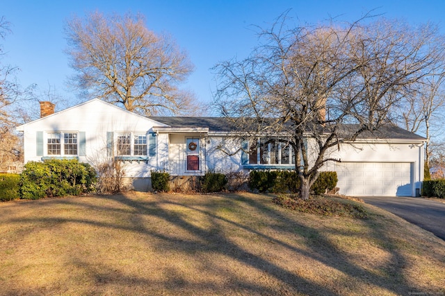 ranch-style home featuring aphalt driveway, an attached garage, a chimney, and a front yard