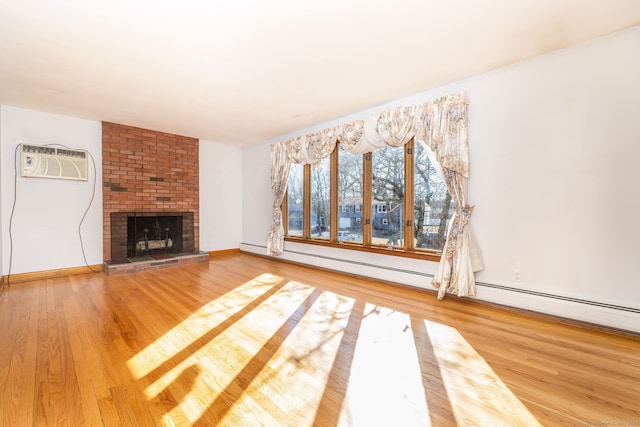 unfurnished living room featuring a fireplace, an AC wall unit, wood finished floors, and baseboards