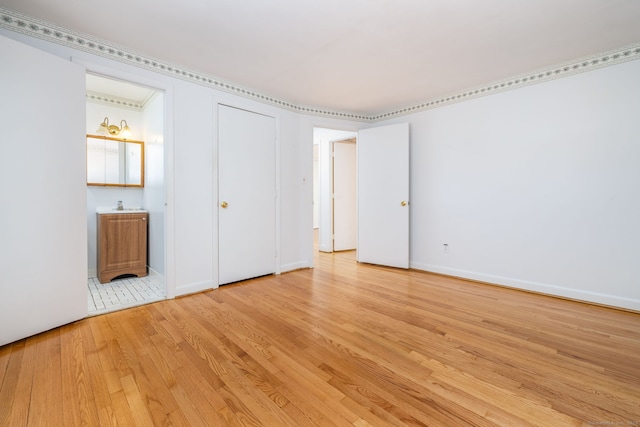 unfurnished bedroom featuring ensuite bath, light wood-style floors, baseboards, and a sink