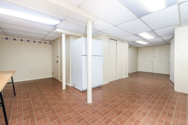 finished basement with brick floor, freestanding refrigerator, and a paneled ceiling