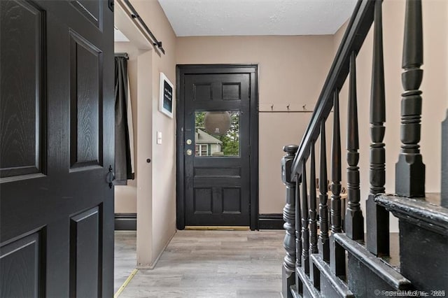 foyer entrance featuring light wood-type flooring, a barn door, a textured ceiling, and stairs