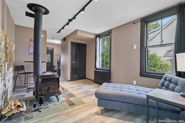 living area featuring a wood stove, light wood-style flooring, radiator heating unit, and a textured ceiling