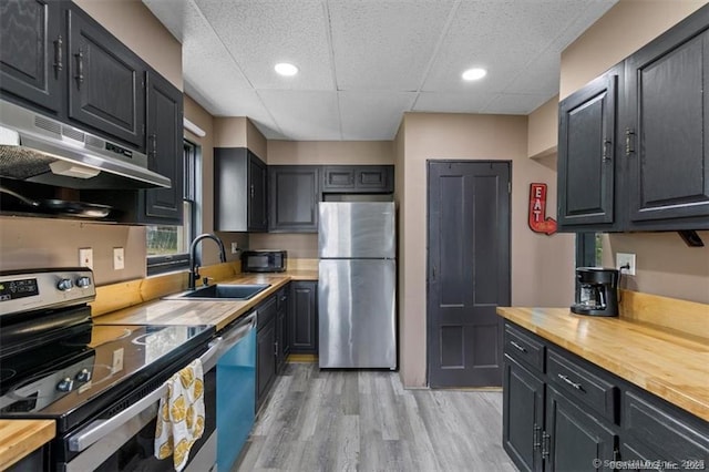 kitchen with light wood-style flooring, appliances with stainless steel finishes, a sink, butcher block countertops, and under cabinet range hood