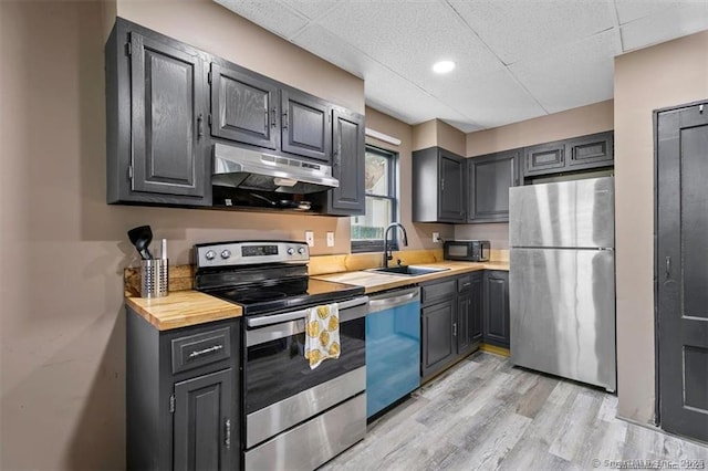 kitchen with light wood finished floors, stainless steel appliances, a paneled ceiling, a sink, and under cabinet range hood